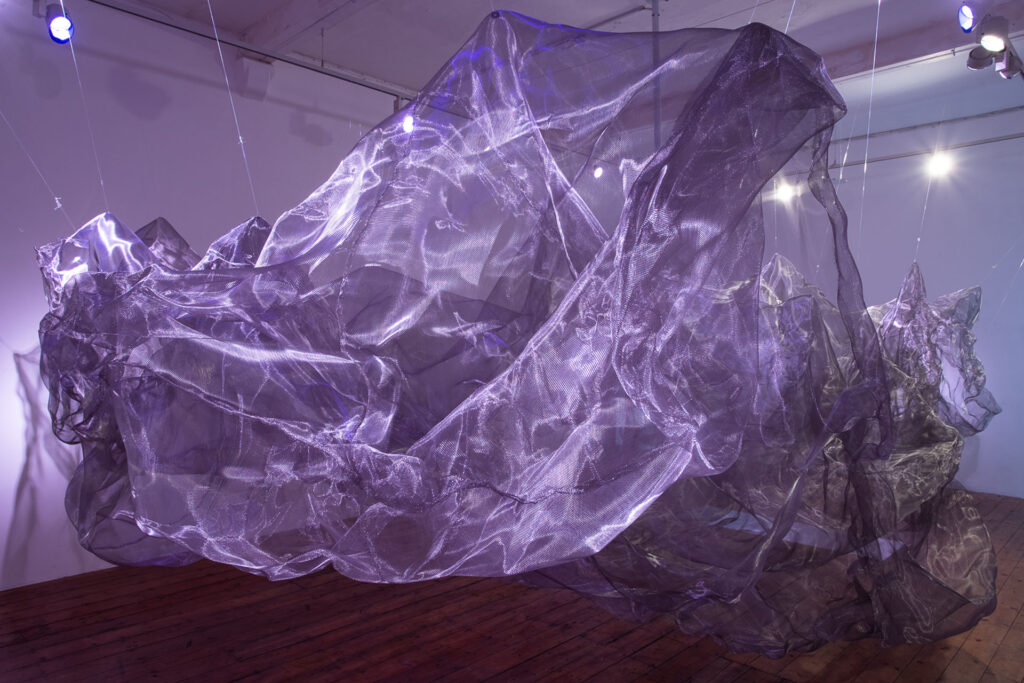 A large mesh installation lit by a purple light takes up an entire room of the Nunnery Gallery