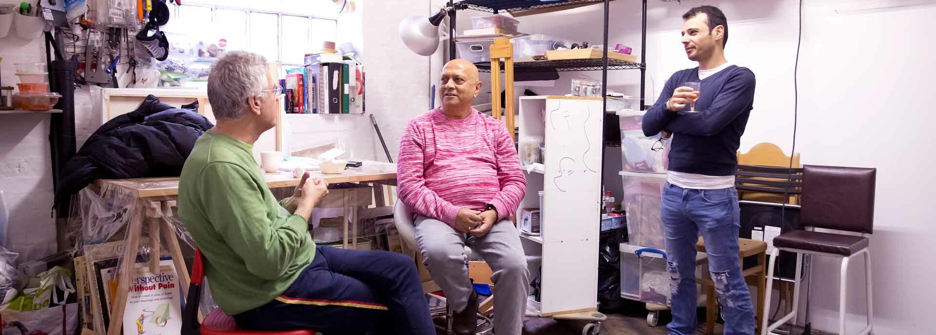 Three people sit in an artist's studio