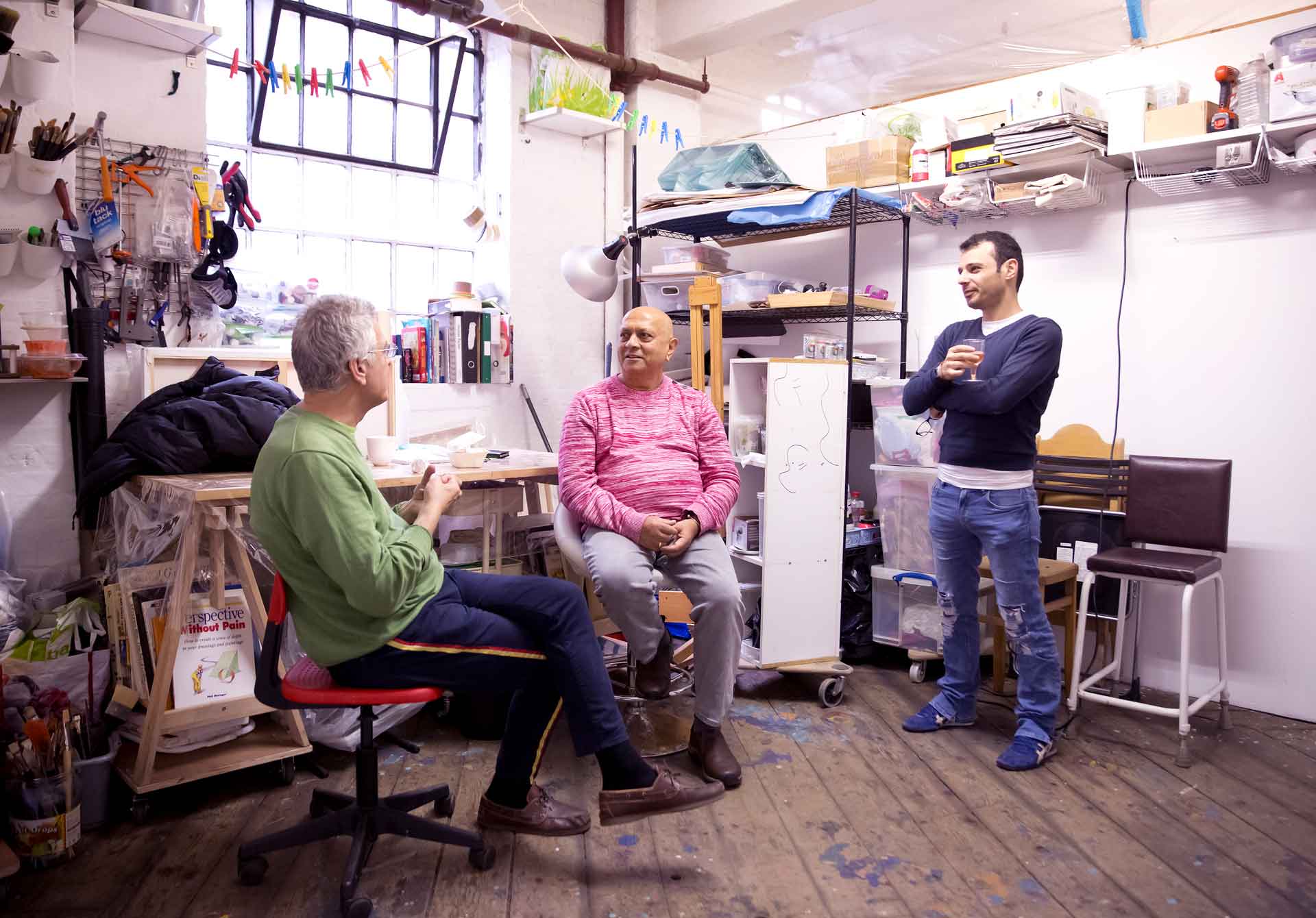 Three people sit in an artist's studio