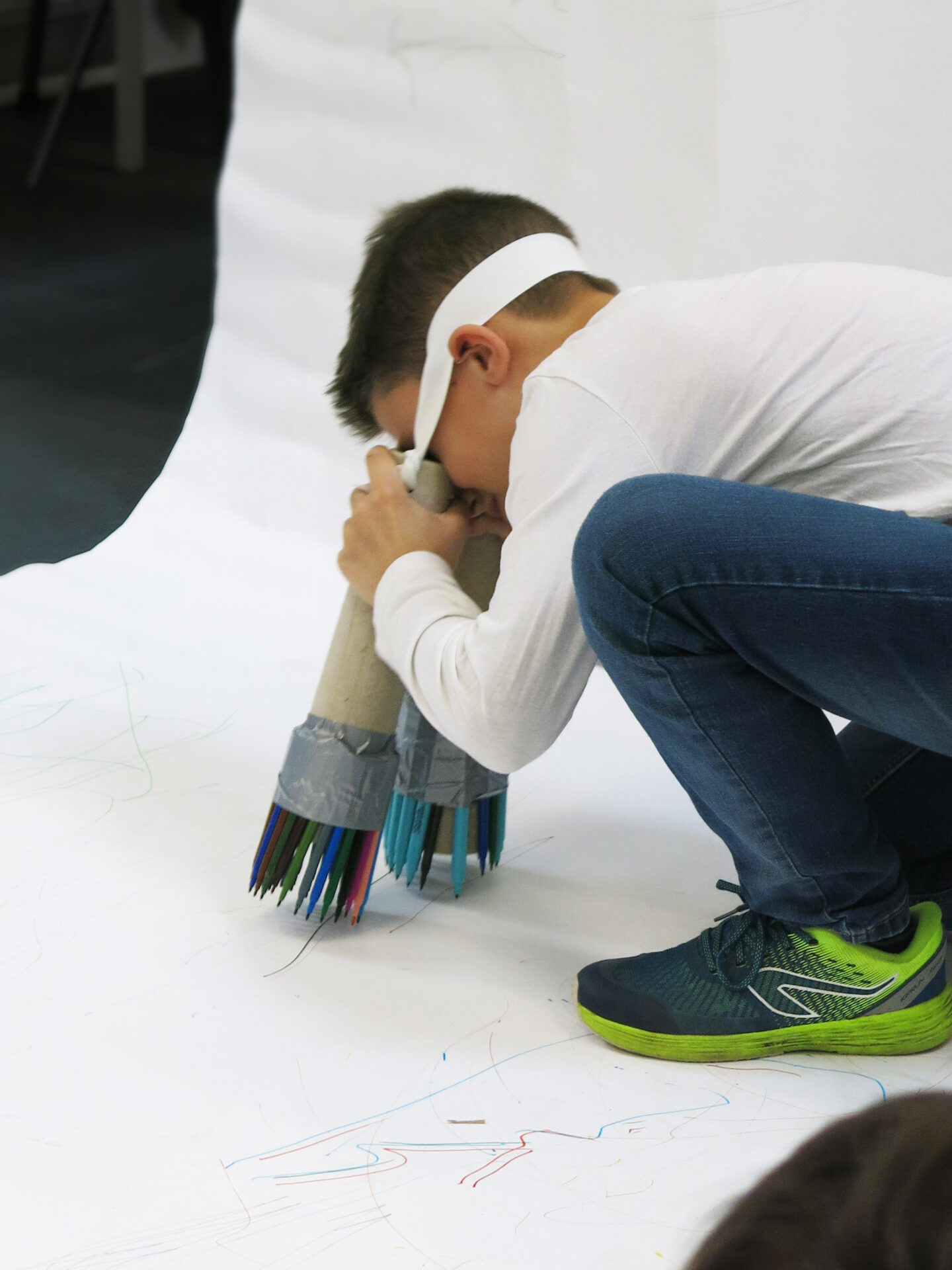 A pupil looks through two carboard tubes with pens on the end and draws on a large piece of paper