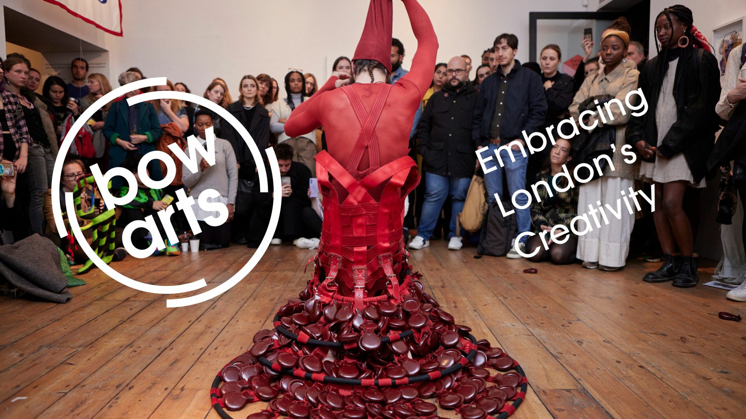 Spectators observe a performance of a person undressing from a castanet dress, the Bow Arts Logo is on the left of the image, Embracing London's Creativity is written on the right
