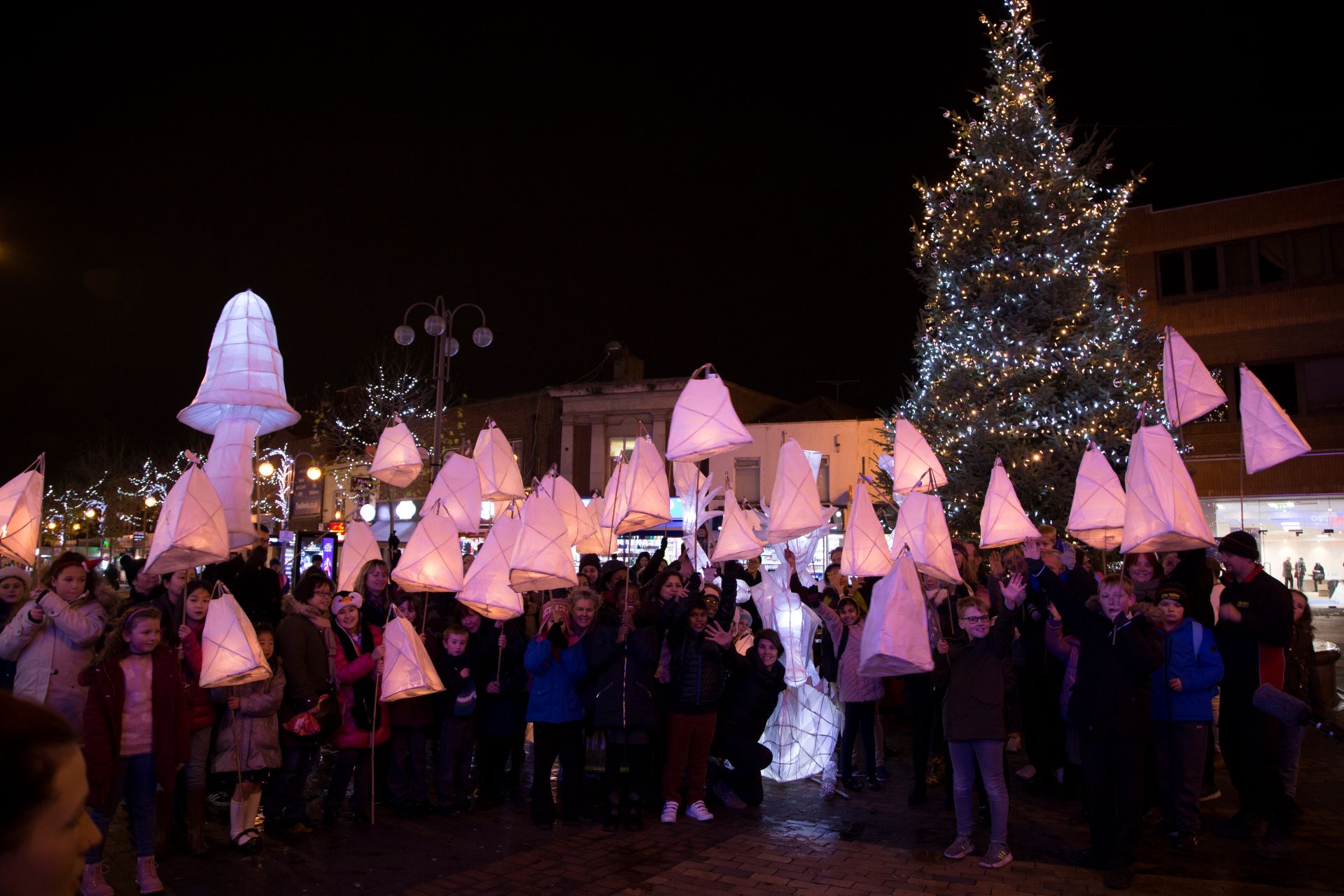 Children hold up lit-up lanterns they made, outside in the dark