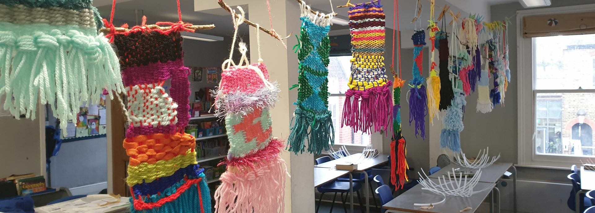 Textile pieces of woven yarn hang in a classroom