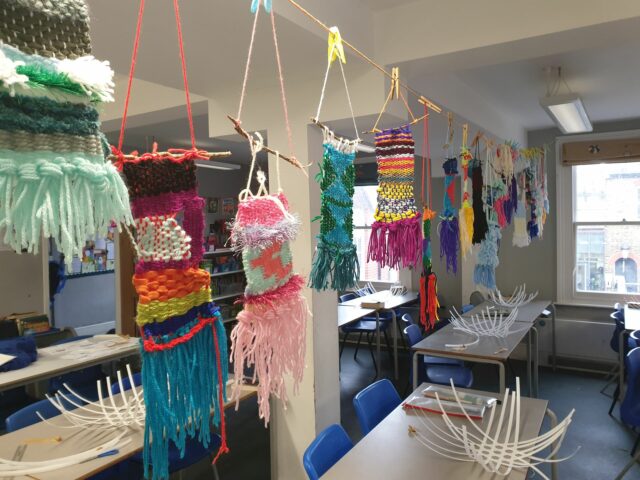 Textile pieces of woven yarn hang in a classroom