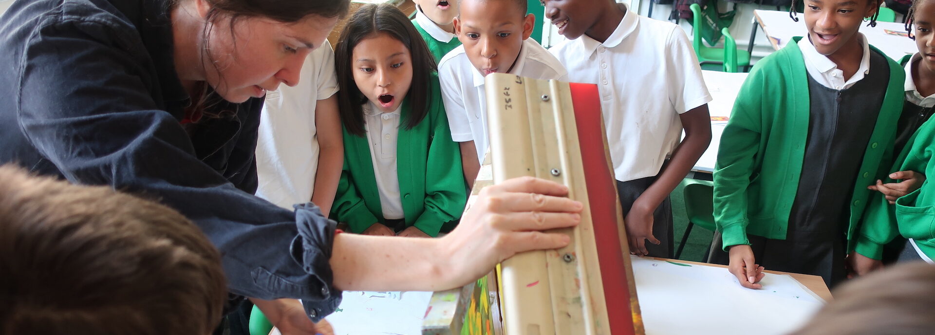 Students look in wonder as an artist educator reveals a print