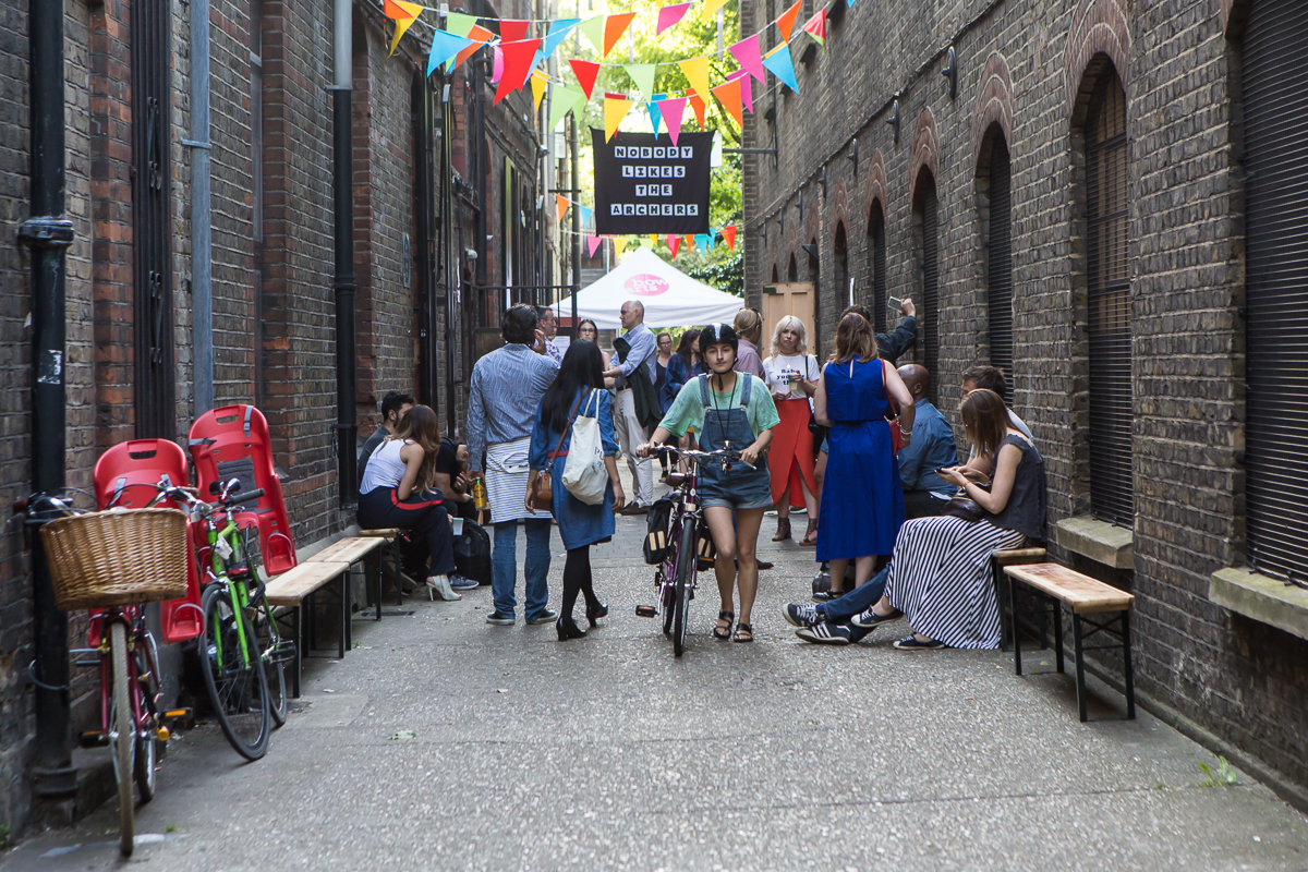 Bow Arts Lane with people gathered around, a banner hangs reading 'Nobody likes the archers'