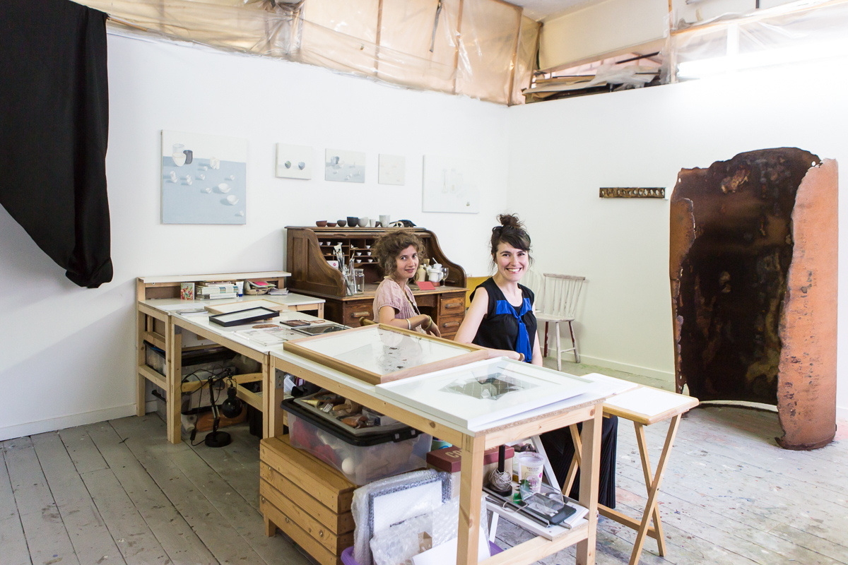 Two people sat down, turn around to smile at the camera in a studio