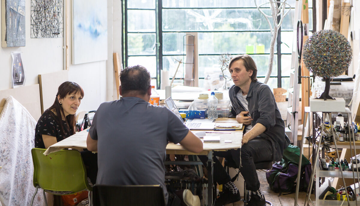 Three people sit at a table in a studio talking