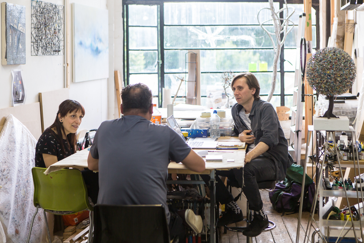 Three people sit at a table in a studio talking