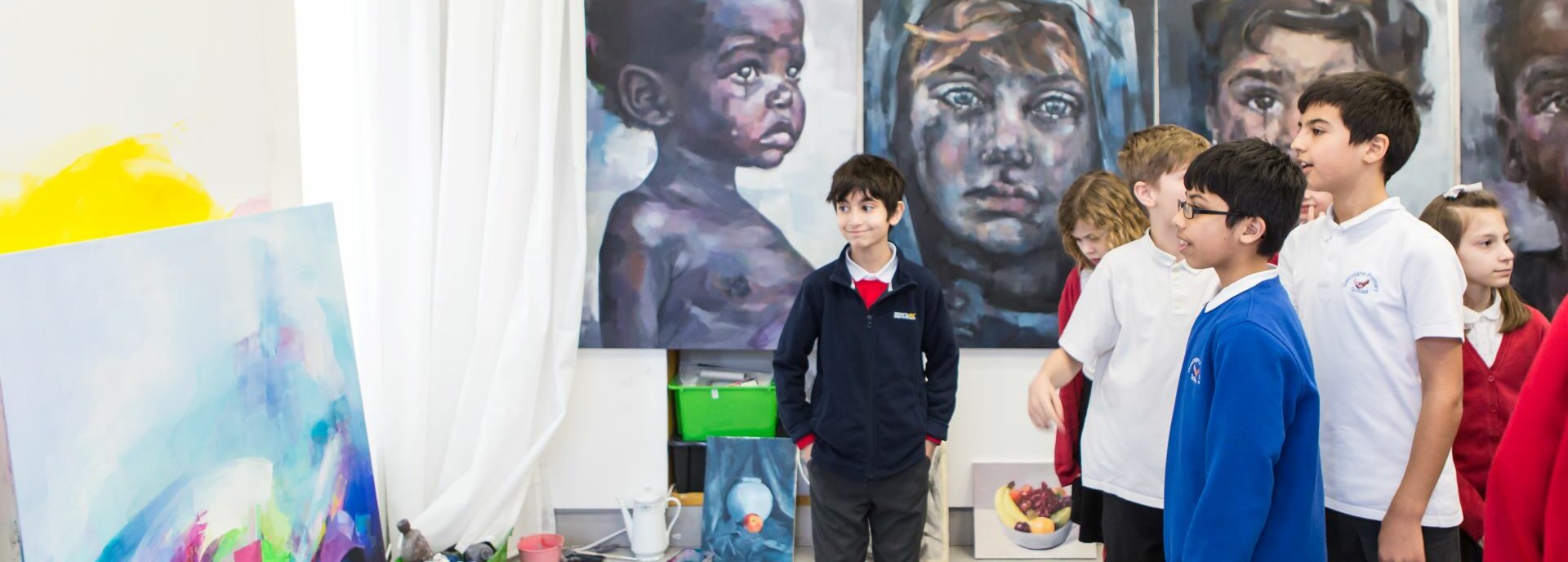 Children look at an abstract painting in an artist's studio, behind them our four paintings of children
