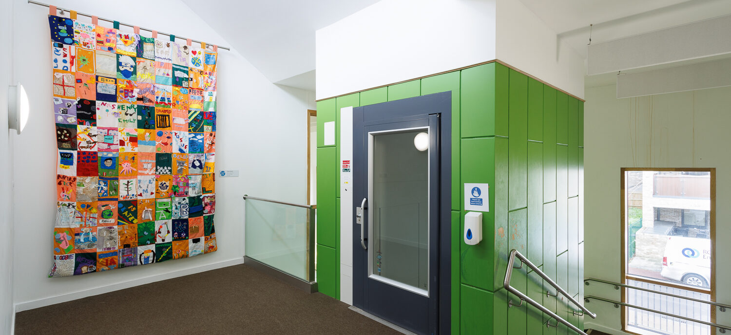 An image of a school stairwell with a quilt created by students hanging from the wall
