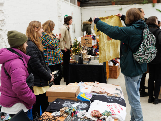 At a t-shirt stall a person holds up a product while the sellers look on