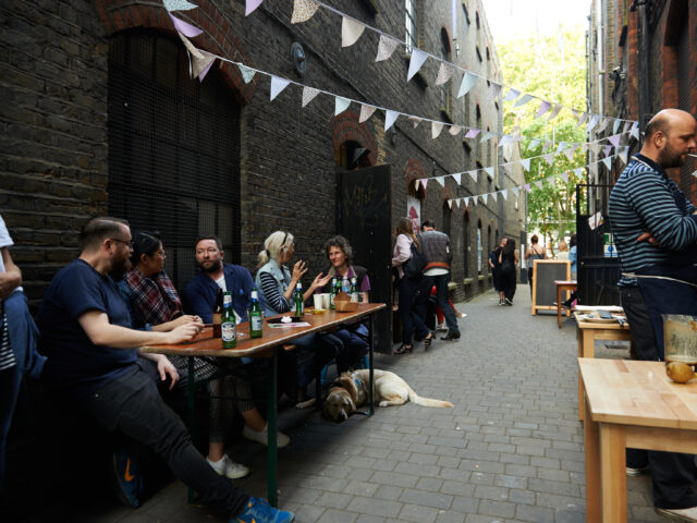 People sit at a table with food and drink in an allyway, pastel bunting is overhead