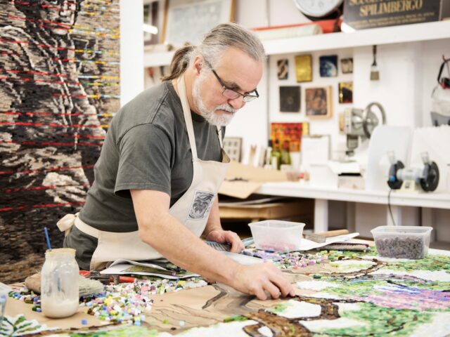 An artist lays mosaic pieces in their studio