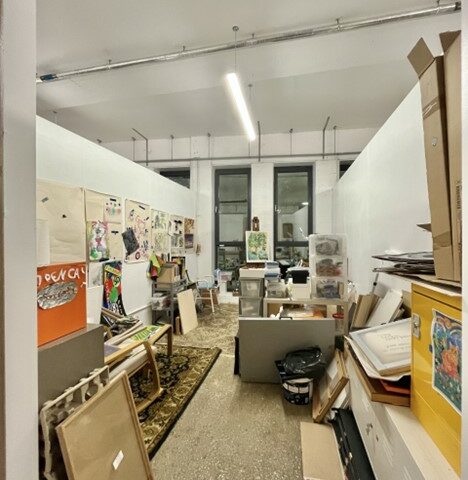 A studio with two windows on the far wall, it is filled with canvases and frames