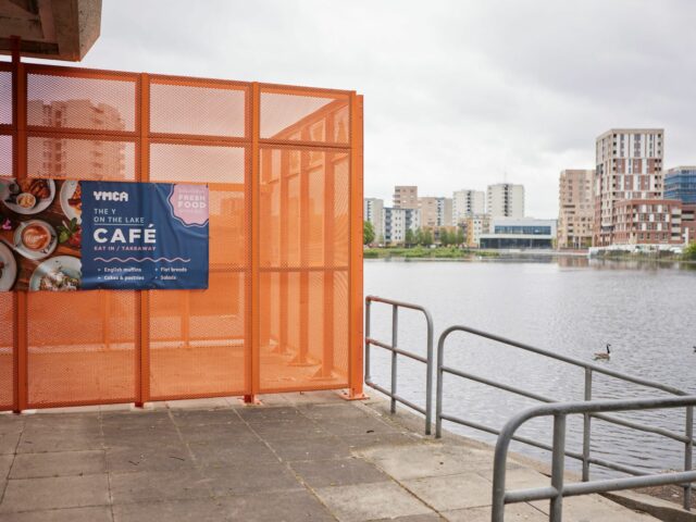 An orange fence has a café banner on next to Southmere lake