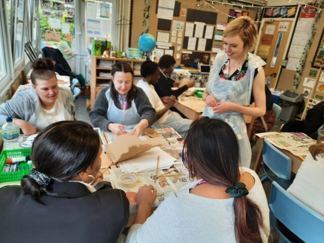 Artist educator looks on as teacher's cut cardboard