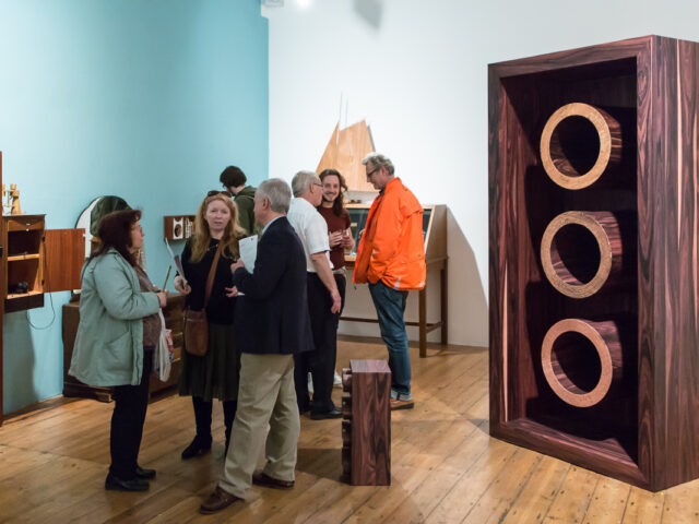 People talk in the gallery surrounded by artworks inspired by and made from wood