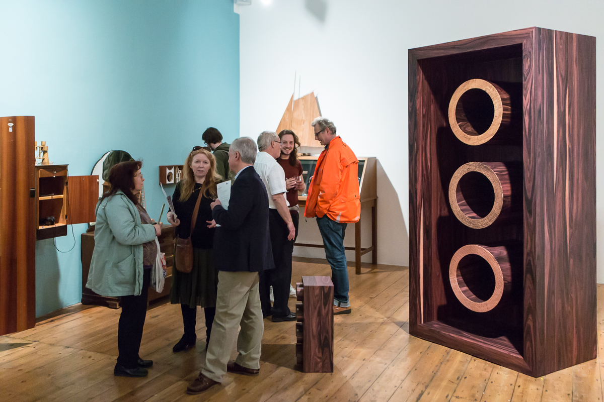 People talk in the gallery surrounded by artworks inspired by and made from wood