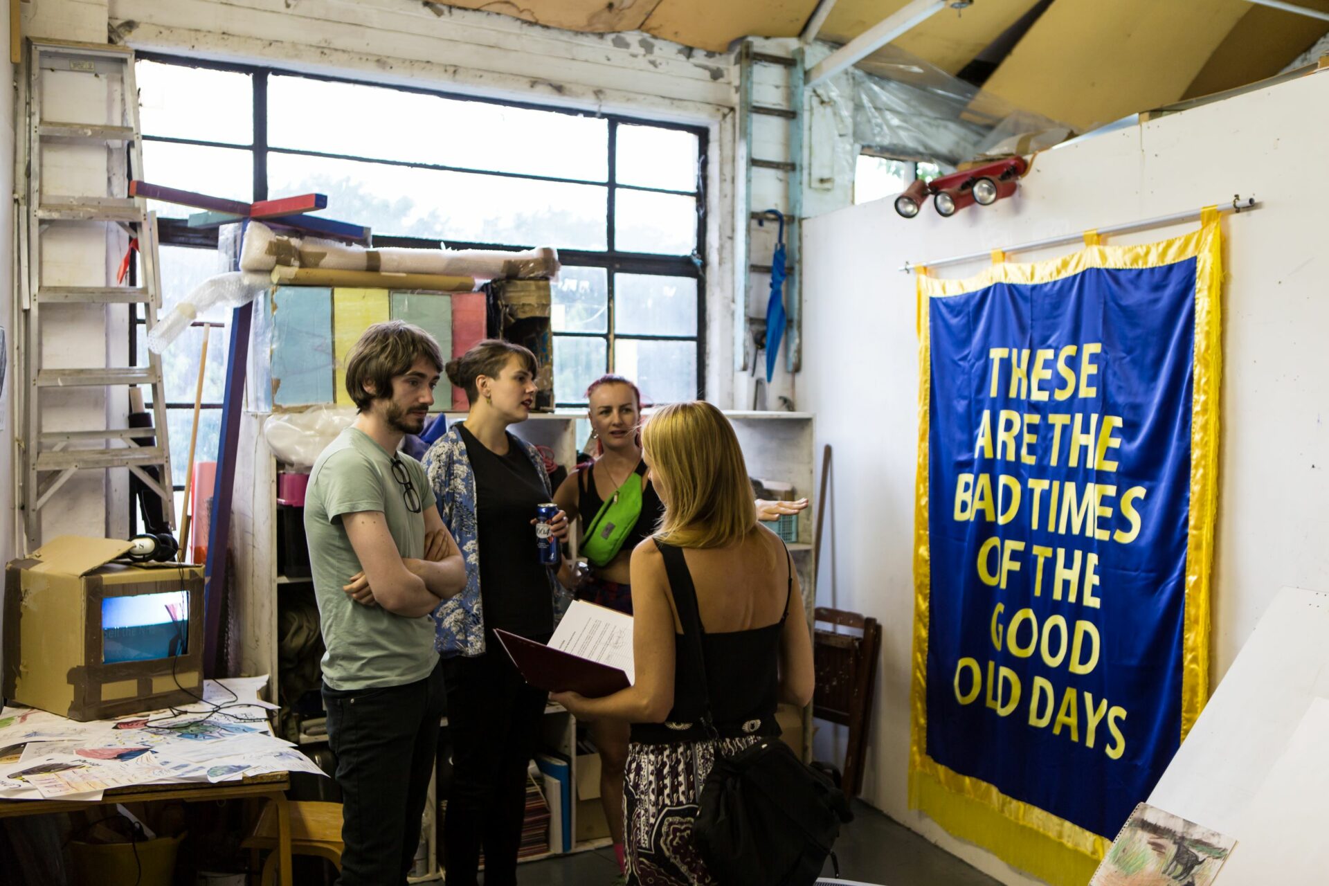 An artist talks to people in their studio, a banner hangs on the wall next to them