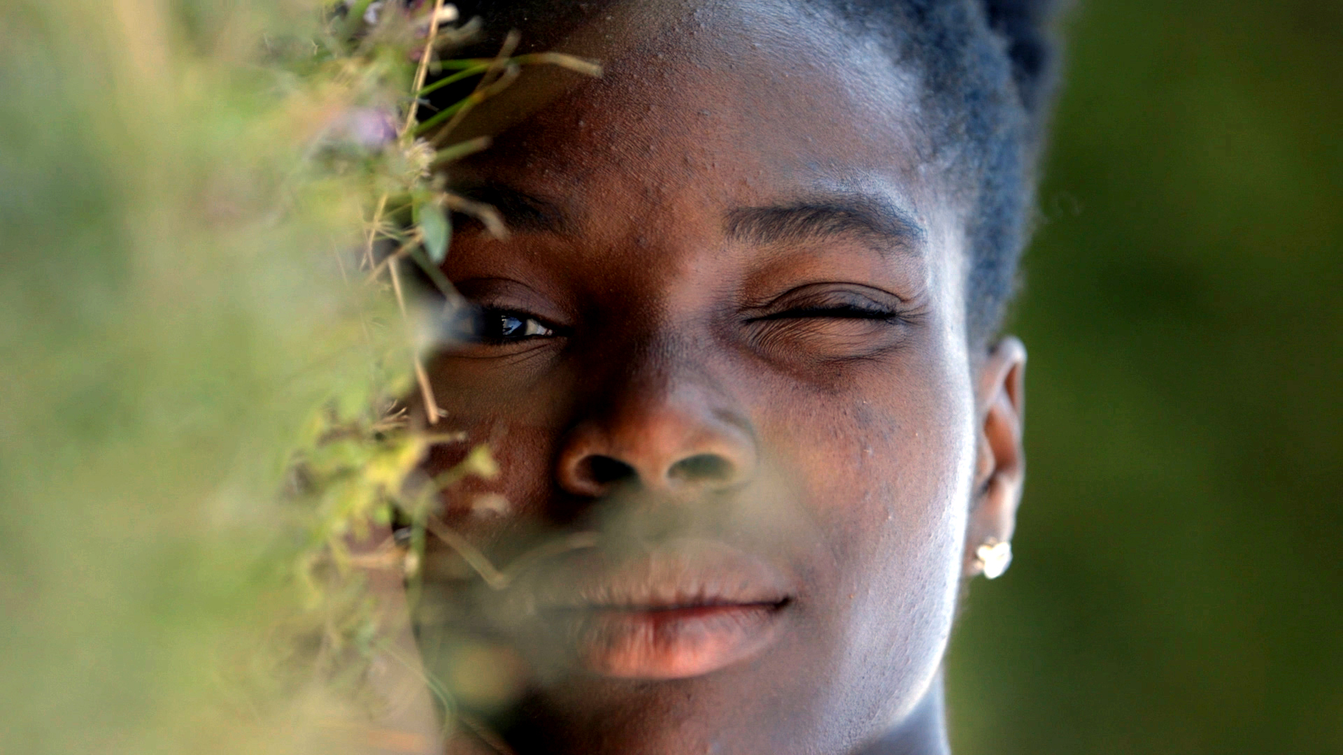 A person holds one eye closed leaning up against grass