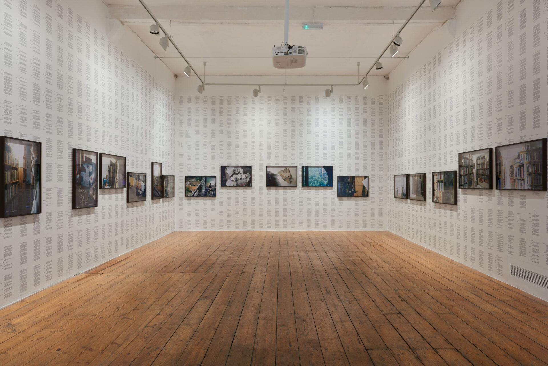 Photographs of a poet's lived spaces are installed on walls papered with words