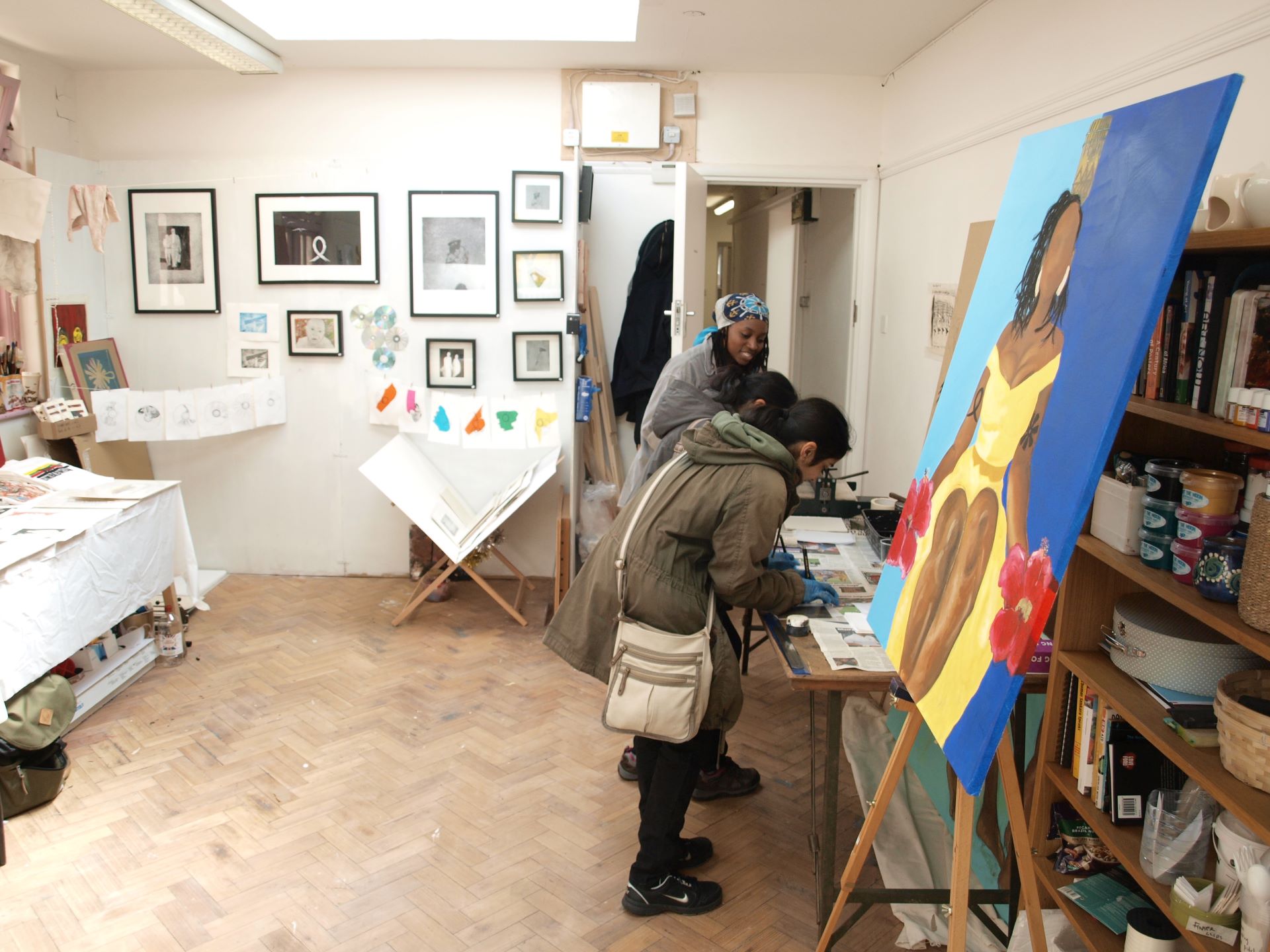 Three people lean over a desk to take part in drawing in a studio, surrounded by the artists work
