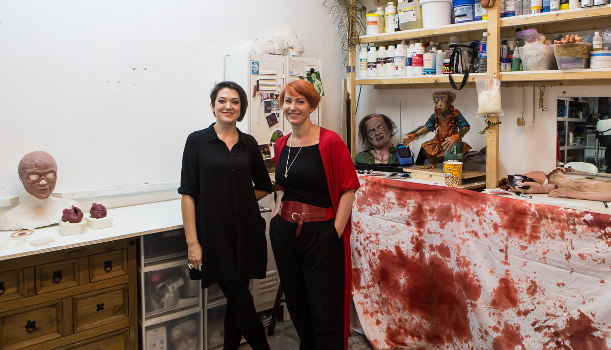 Two people stand in a studio, behind them are fake prosthetics