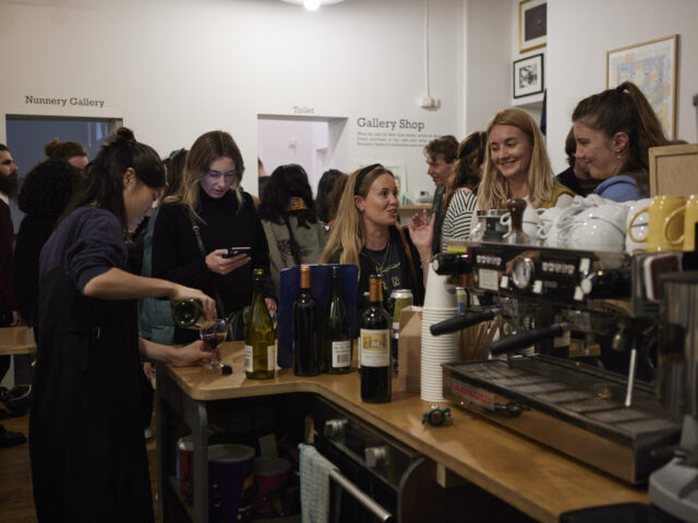 people gather round a café bar as a bar tender pours wine