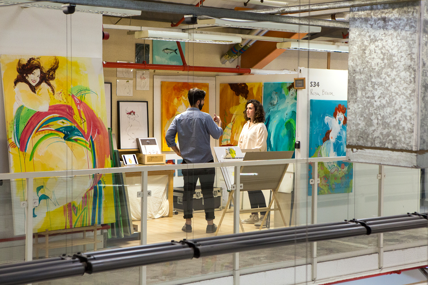 Two people stand in a studio surrounded by paintings