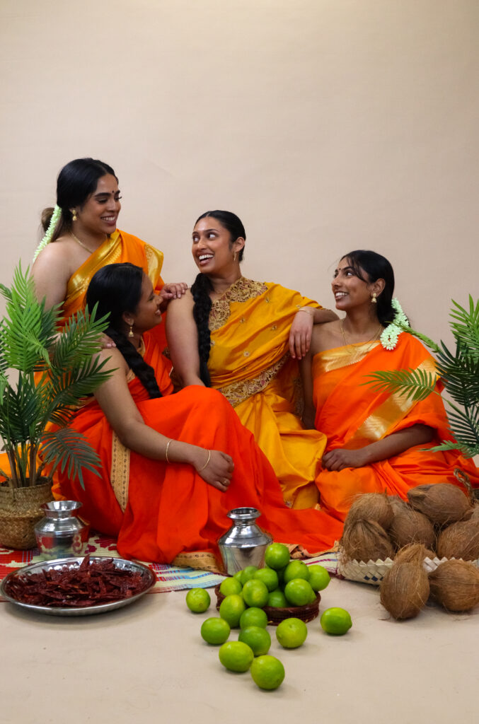 Four young women in orange clothing next to bowls and platters of limes, coconuts, and chillis.