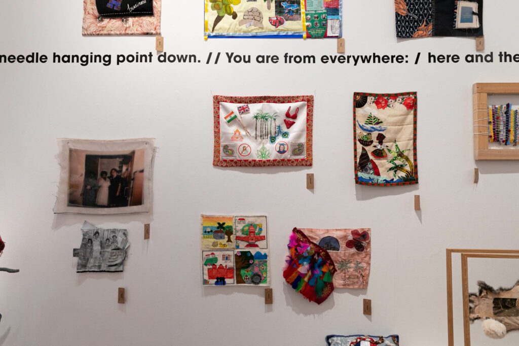 A variety of cloths with a line of Nathalie Abi-Ezzi's poetry on the wall: "needle hanging point down.// You are from everywhere: / here and there