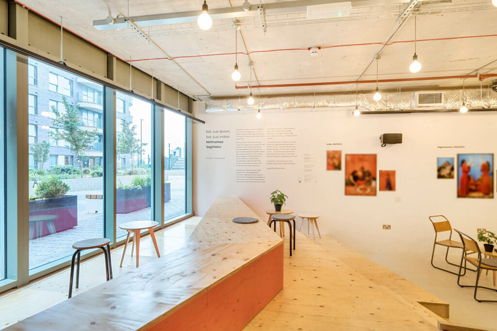 Image overlooks well-lit section of café, including front windows, large wood steps, and section of gallery exhibit. 