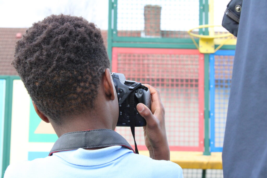 Back of a boy's head looking though the viewfinder of a camera taking a picture in a school playground.